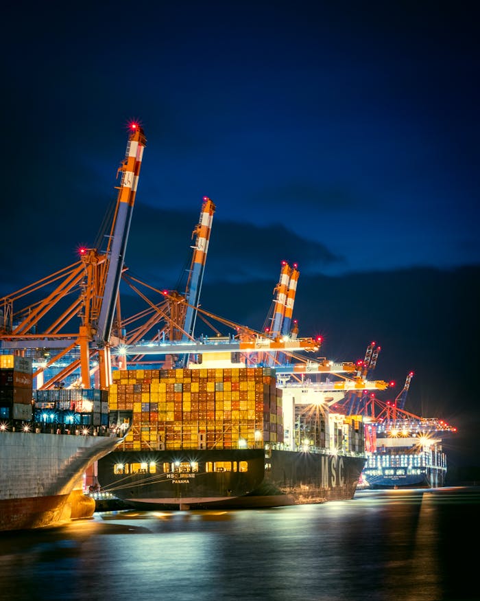 about-01 Vibrant night view of container ships at Hamburg port with cranes illuminated.